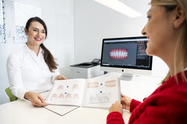 Zahnärztin berät Patientin mit Zahndiagramm und digitaler Zahnvisualisierung am Computer.