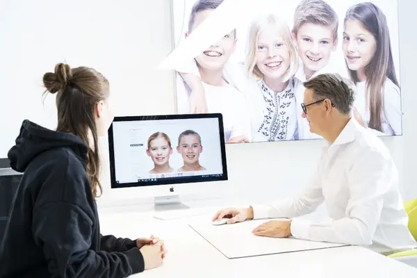 Kieferorthopäde berät Jugendliche am Computer mit digitaler Zahnkorrektur-Visualisierung.