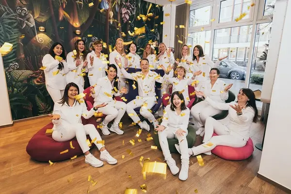 Ein fröhliches Praxisteam in weißer Kleidung wirft goldene Konfetti in moderner Zahnarztpraxis.