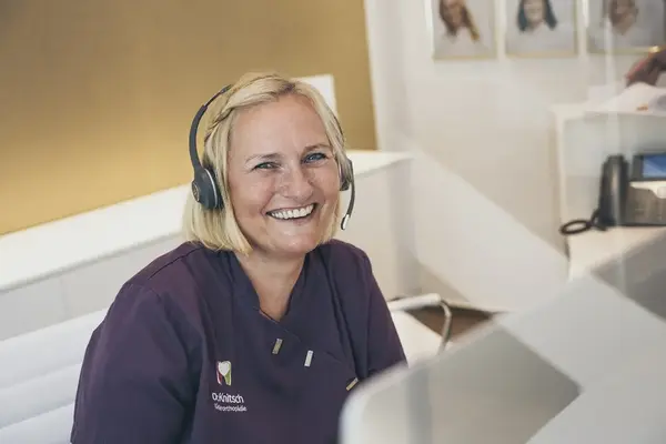 Freundliche Mitarbeiterin einer Kieferorthopädie am Empfang mit Headset berät Patienten.