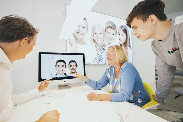 Drei Menschen besprechen am Computer in einer modernen Zahnarztpraxis Behandlungsfotos.