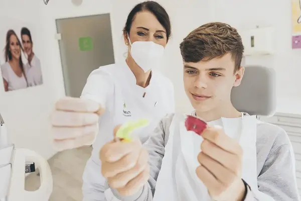 Jugendlicher sitzt beim Kieferorthopäden und betrachtet verschiedene Zahnspangenmodelle.