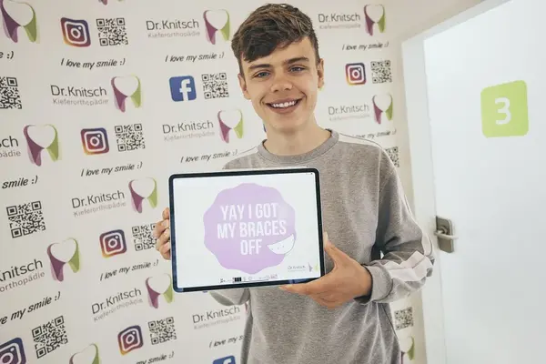 Junger Patient freut sich in Kieferorthopädie-Praxis nach Zahnspangen-Entfernung.