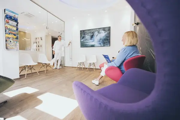 Modernes, helles Wartezimmer einer Zahnarztpraxis mit Patientin und freundlichem Zahnarzt.